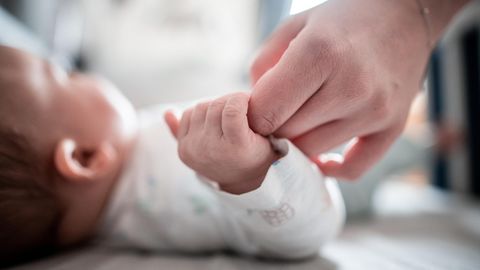 Ein Baby klammert sich an den Finger seiner Mutter