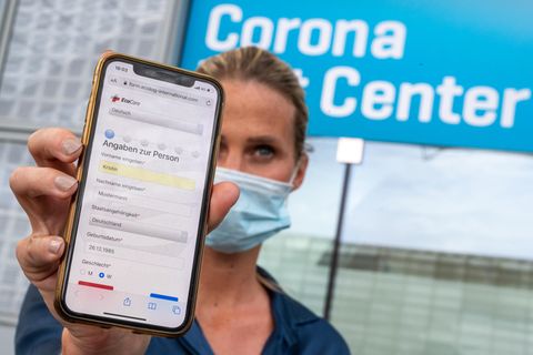 Eine Frau hält ihr Smartphone in die Kamera, mit dem sie sich zuvor am Flughafen für den Coronatest angemeldet hat.