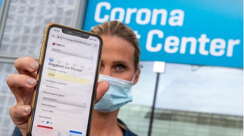 Eine Frau hält ihr Smartphone in die Kamera, mit dem sie sich zuvor am Flughafen für den Coronatest angemeldet hat.