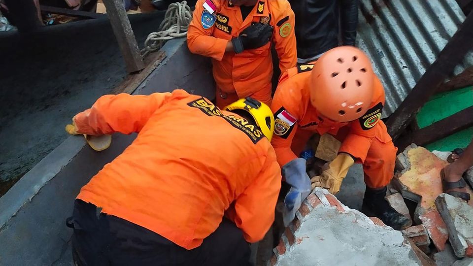 Indonesien Erdbeben Sulawesi Rettungstrupp Suchtrupp Drei Männer in orangen Overalls und Helmen knien auf den Trümmern eines Gebäudes und schauen durch einen Spalt ins Dunkel