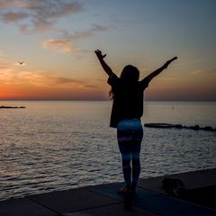 Eine Frau steht vor dem Meer und wirft die Arme hoch