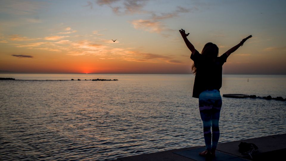 Eine Frau steht vor dem Meer und wirft die Arme hoch