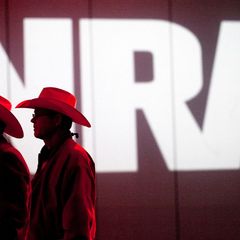 Zwei Männer mit Cowboyhüten stehen vor dem Logo der NRA