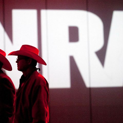 Zwei Männer mit Cowboyhüten stehen vor dem Logo der NRA