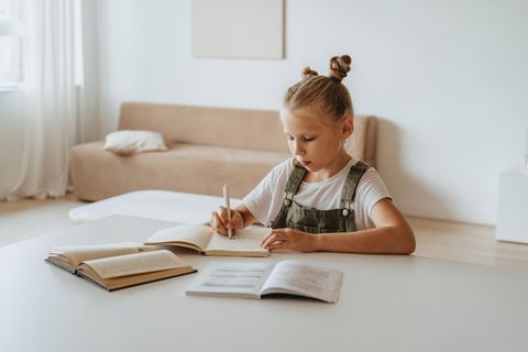 Ein kleines Mädchen sitzt zuhause über Schulbüchern