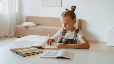 Ein kleines Mädchen sitzt zuhause über Schulbüchern