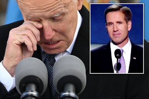 In schwarzem Mantel und Krawatte steht Joe Biden vor zwei Mikrofonen und wischt sich mit der rechten Hand eine Träne ab