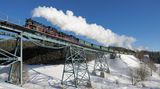 An einem Wintertag mit strahlender Sonne und blauem Himmel: Der lange Zug wird von zwei Lokomotiven gezogen.