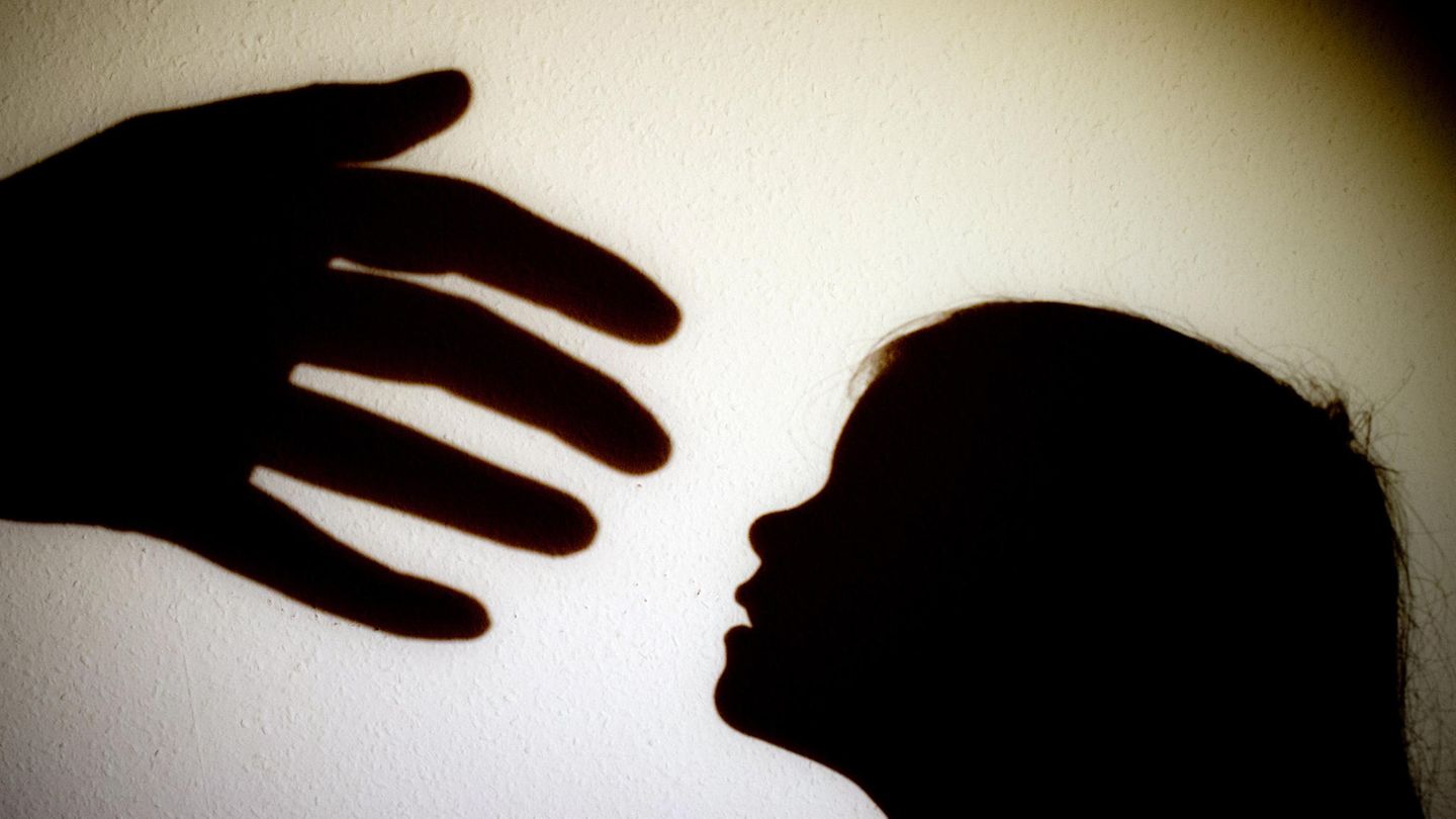 Schatten einer Hand einer erwachsenen Person und der Kopf eines Kindes an einer Wand eines Zimmers.