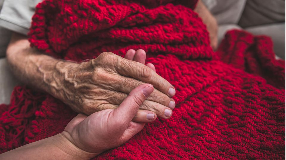 Pflege: Eine Frau hält die Hand eines älteren Mannes