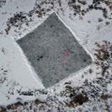 Farbklecks auf einer vom Schnee freigeräumten Eisfläche in Ruderatshofen, Bayern, mit einem rot gekleideten Schlittschuhläufer