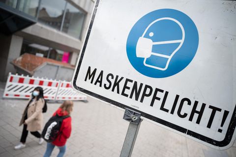 Zwei Passantinnen gehen in einer Fußgängerzone hinter einem Schild vorbei, auf dem "Maskenpflicht" steht