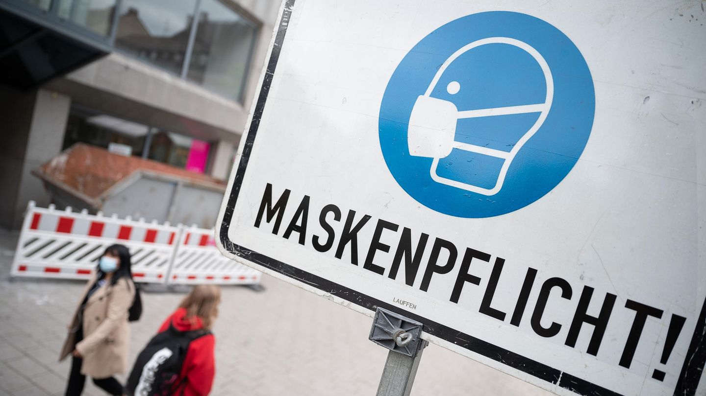 Zwei Passantinnen gehen in einer Fußgängerzone hinter einem Schild vorbei, auf dem "Maskenpflicht" steht