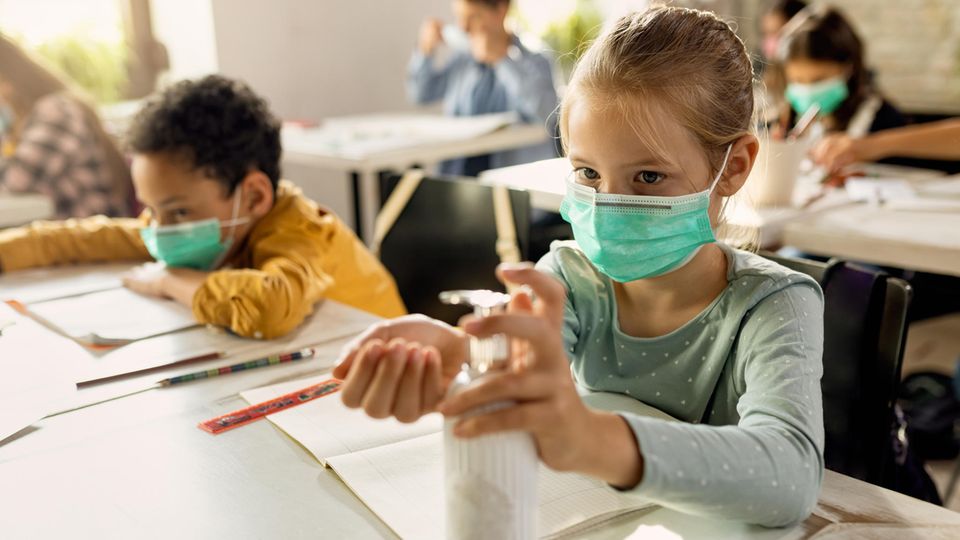 Kinder in einem Klassenzimmer mit Masken und Desinfektionsmittel