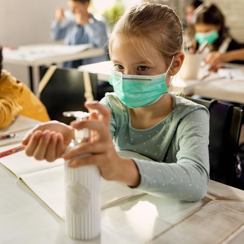 Kinder in einem Klassenzimmer mit Masken und Desinfektionsmittel