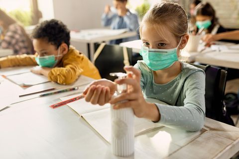 Kinder in einem Klassenzimmer mit Masken und Desinfektionsmittel