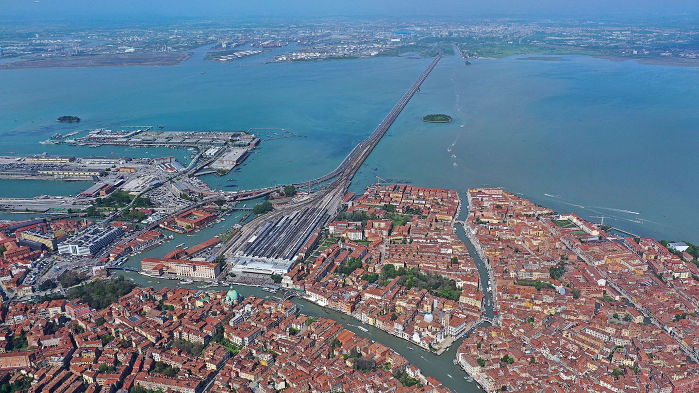 Stationen des Aufbruchs: Venedig – Italien Diese Luftaufnahme zeigt Venedig und den Hauptbahnhof Santa Lucia. Er ist ein Kopfbahnhof und der einzige Bahnhof auf der Insel von Venedig. Seinen Namen hat er von der Santa-Lucia-Kirche, die ursprünglich an diesem Ort stand und für den Bau des Bahnhofs 1861 abgerissen wurde. Über den Ponte della Libertà ist der Bahnhof mit dem Knotenbahnhof Venezia Mestre auf dem Festland verbunden. Venedig – Italien Diese Luftaufnahme zeigt Venedig und den Hauptbahnhof Santa Lucia. Er ist ein Kopfbahnhof und der einzige Bahnhof auf der Insel von Venedig. Seinen Namen hat er von der Santa-Lucia-Kirche, die ursprünglich an diesem Ort stand und für den Bau des Bahnhofs 1861 abgerissen wurde. Über den Ponte della Libertà ist der Bahnhof mit dem Knotenbahnhof Venezia Mestre auf dem Festland verbunden.