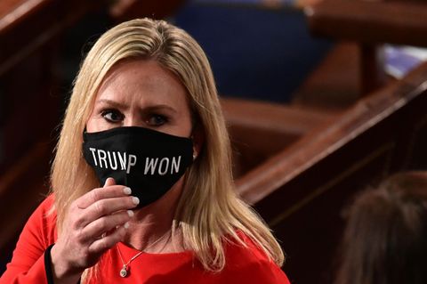 Eine blonde, mittelalte Frau in rotem Oberteil fasst an ihren schwarzen Mund-Nasen-Schutz mit weißem "Trump won"-Schriftzug