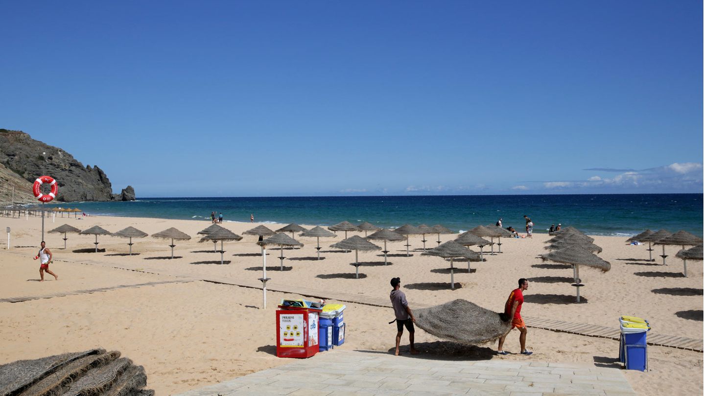 An der Praia Da Luz: Zwei Männer räumen am Strand der portugiesischen Algarveküste die Sonnenschirme ab.