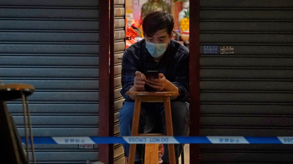 Ein Mann vertreibt sich die Zeit mit seinem Smartphone, während er auf sein Corona-Testergebnis wartet. Bewohner im gesperrten Bereich des Honkonger Bezirks Sham Shui Po sind verpflichtet, über Nacht zu Hause zu bleiben, bis sie einen negativen Corona-Test vorweisen können.