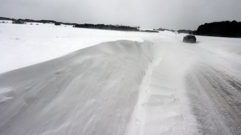 Ein Auto fährt über eine von Schneeverwehungen bedeckte Landstraße