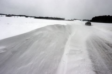 Ein Auto fährt über eine von Schneeverwehungen bedeckte Landstraße