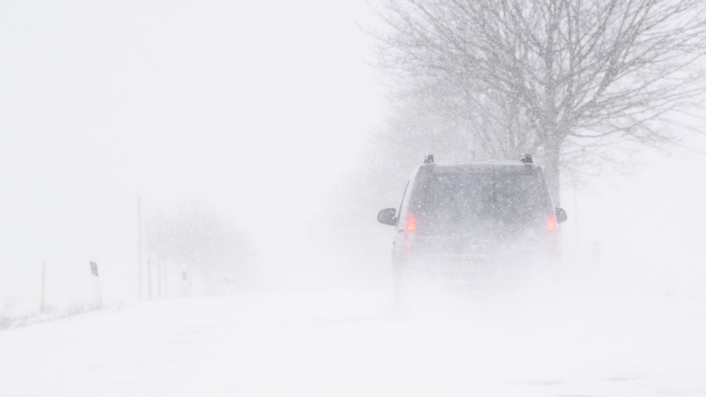 Ein Auto fährt bei Schneesturm über eine Landstraße.
