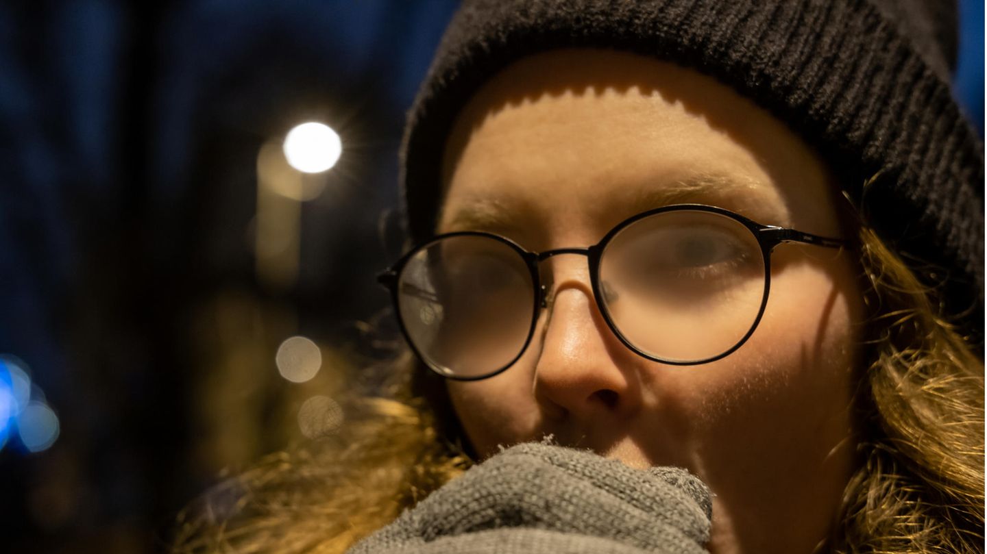 Mädchen warten draußen in den kalten, wärmenden Händen, ihre Brille wird neblig.