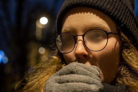 Mädchen warten draußen in den kalten, wärmenden Händen, ihre Brille wird neblig.