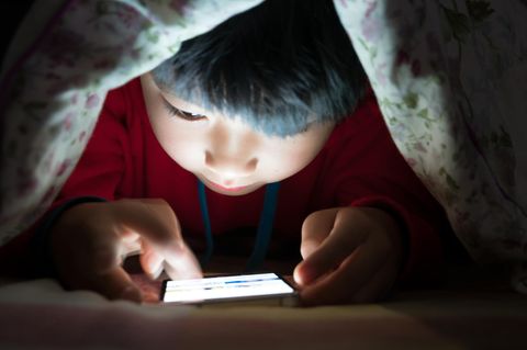Kind unter einer Decke am Smartphone