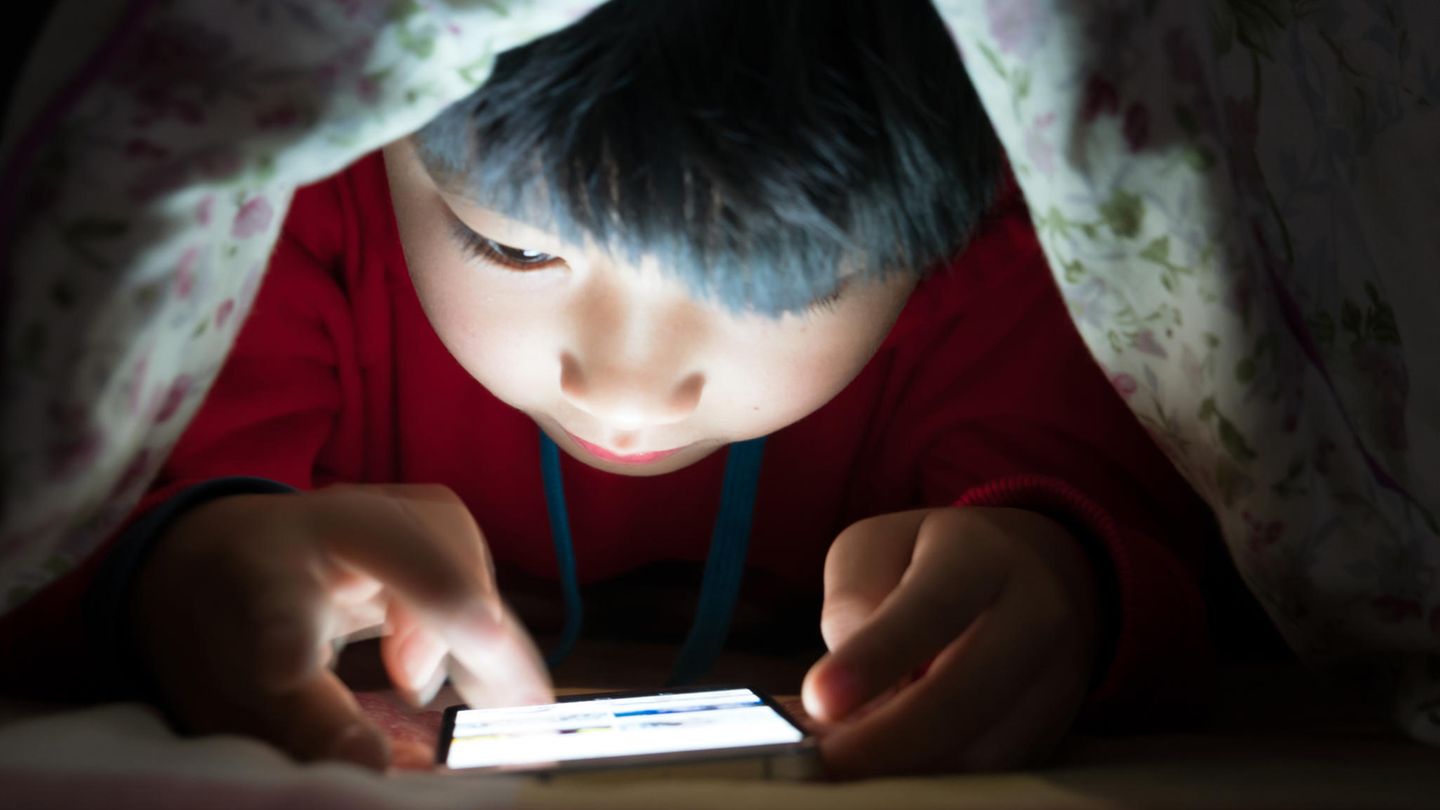 Kind unter einer Decke am Smartphone