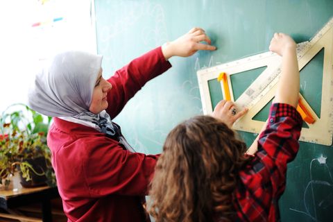 Eine Lehrerin mit Kopftuch steht mit einem Schüler an der Tafel