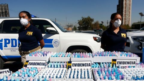 Polizistinnen mit Masken stehen neben beschlagnahmten Flaschen mit Alkohol-Gel, die ohne Genehmigung verkauft wurden