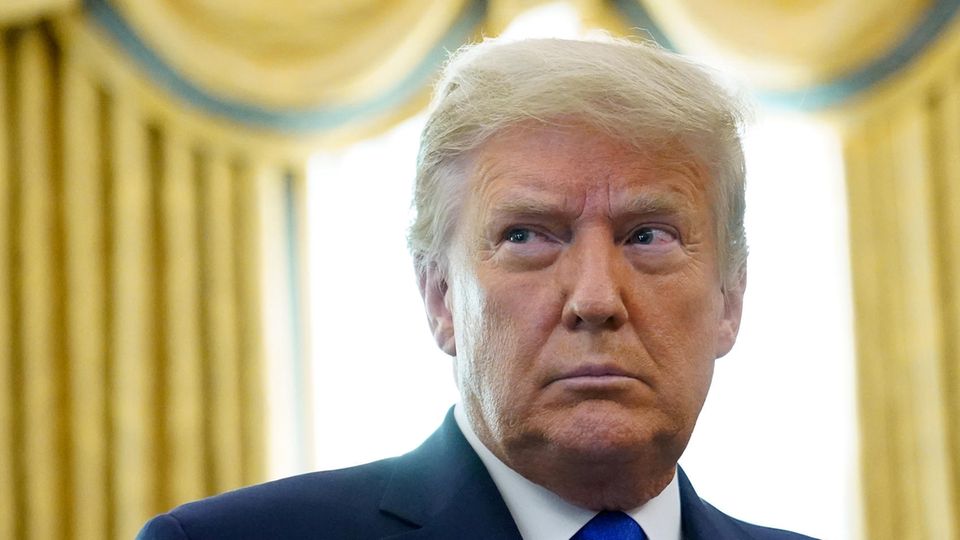 Donald Trump Donald Trump steht im Anzug im Oval Office vor einem Fenster mit goldenen Vorhängen