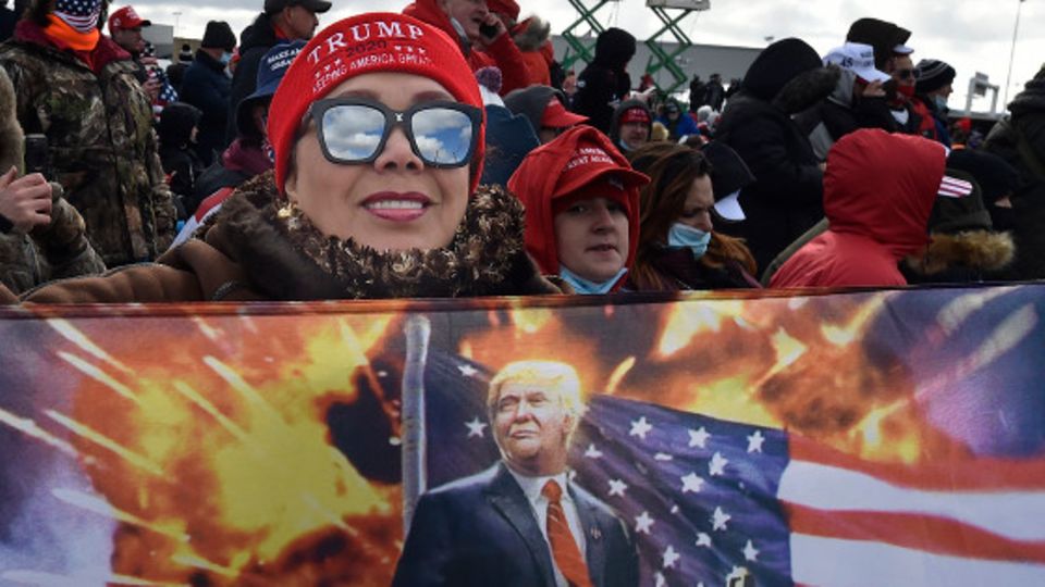 Eine Frau hält bei einer Wahlkampfveranstaltung eine Fahne auf der Ex-US-Präsident Trump zu sehen ist