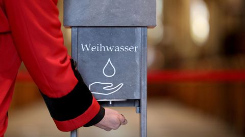 Eine Person hält ihre Hand unter einen kontaktlosen Weihwasserspender