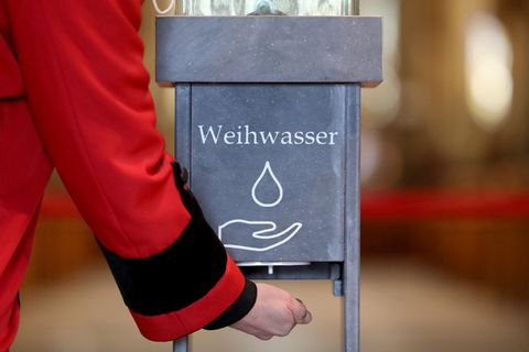 Eine Person hält ihre Hand unter einen kontaktlosen Weihwasserspender