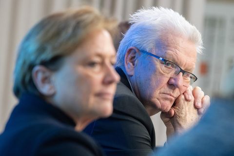 Winfried Kretschmann schaut ernst zur Seite in die Kamera, davor, unscharf: CDU-Herausforderin Susanne Eisenmann