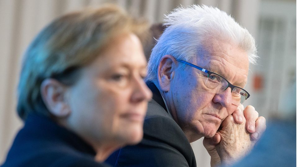 Winfried Kretschmann schaut ernst zur Seite in die Kamera, davor, unscharf: CDU-Herausforderin Susanne Eisenmann