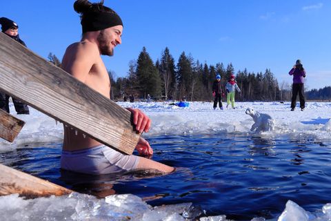 Ein junger Mann steigt im Winter zum Eisbaden in einen halb gefrorenen See.