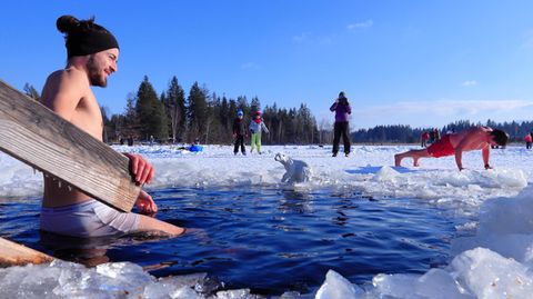 Ein junger Mann steigt im Winter zum Eisbaden in einen halb gefrorenen See.