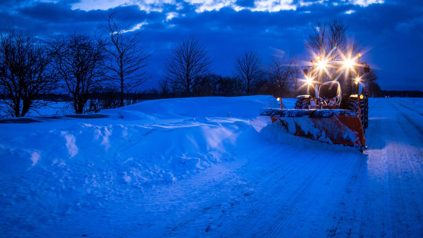 Ein Traktor mit Schneepflug räumt eine Straße frei