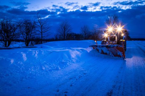 Ein Traktor mit Schneepflug räumt eine Straße frei