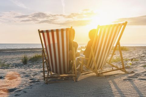 Urlauber sitzen in Liegestühlen an einem Strand