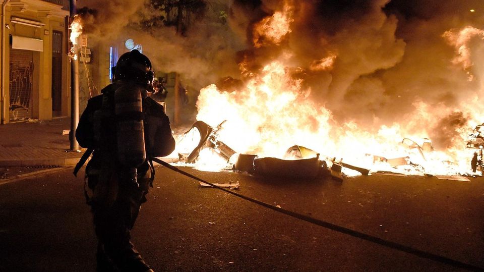 Barcelona Krawall Feuer Barrikaden Feuerwehrmann Ein Feuerwehrmann mit Atemluft-Tank auf dem Rücken nähert sich mit Schlauch in den Händen einem brennenden Auto