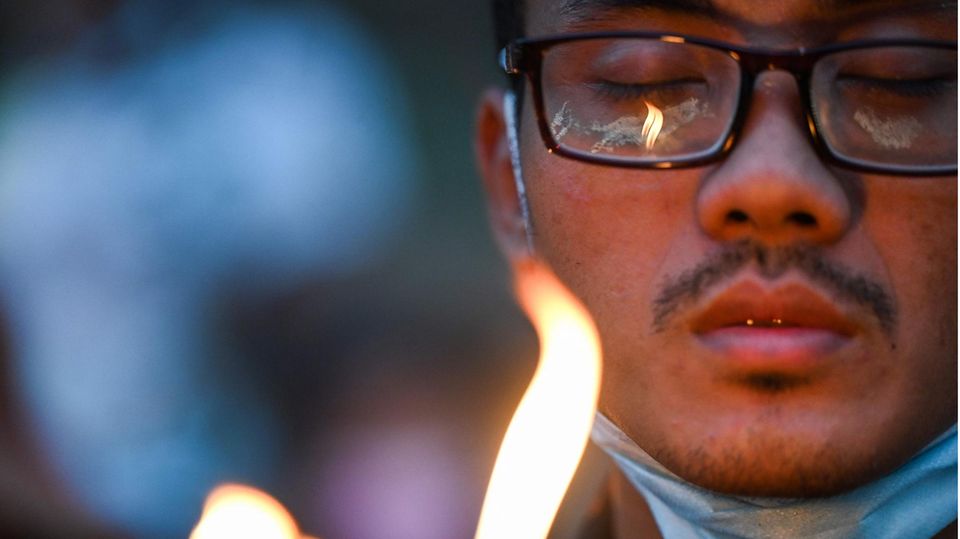 Myanmar Demonstrant Kerze Gebeit Ein Asiate mit schwarzem Brillengestell hält seine Augen geschlossen, während eine Kerzenflamme sein Gesicht erhellt
