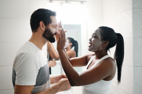 Gesichtscreme für Männer: Eine Frau cremt das Gesicht ihres Partners ein.
