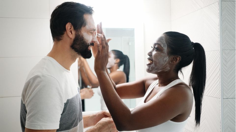 Gesichtscreme für Männer: Eine Frau cremt das Gesicht ihres Partners ein.