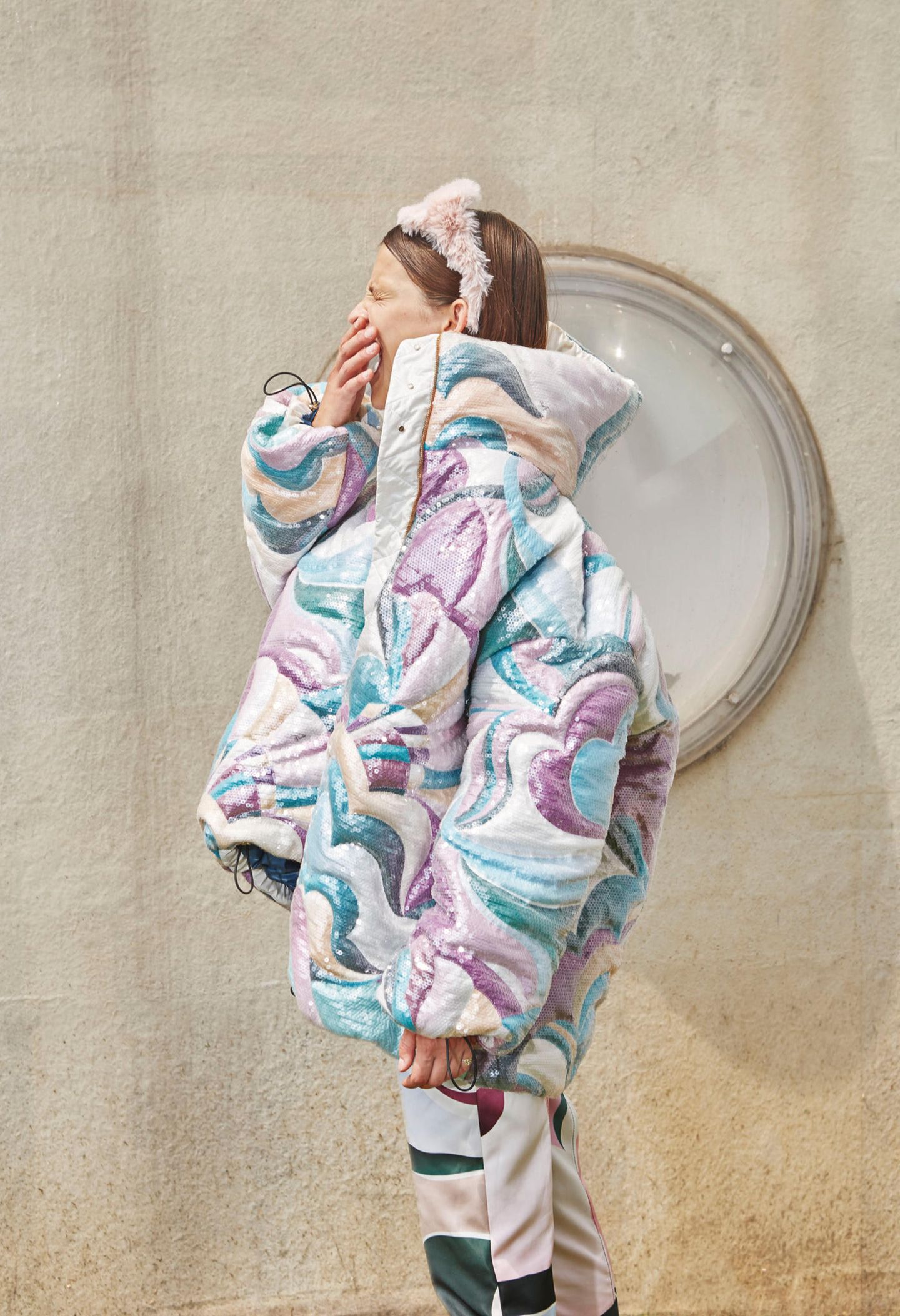 Ein Model trägt eine Daunenjacke mit großem Kragen und hält sich gähnend die Hand vor den Mund