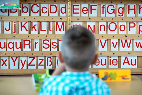 Ein Kind sitzt an einem Tisch; im Hintergrund sind Buchstaben zu sehen